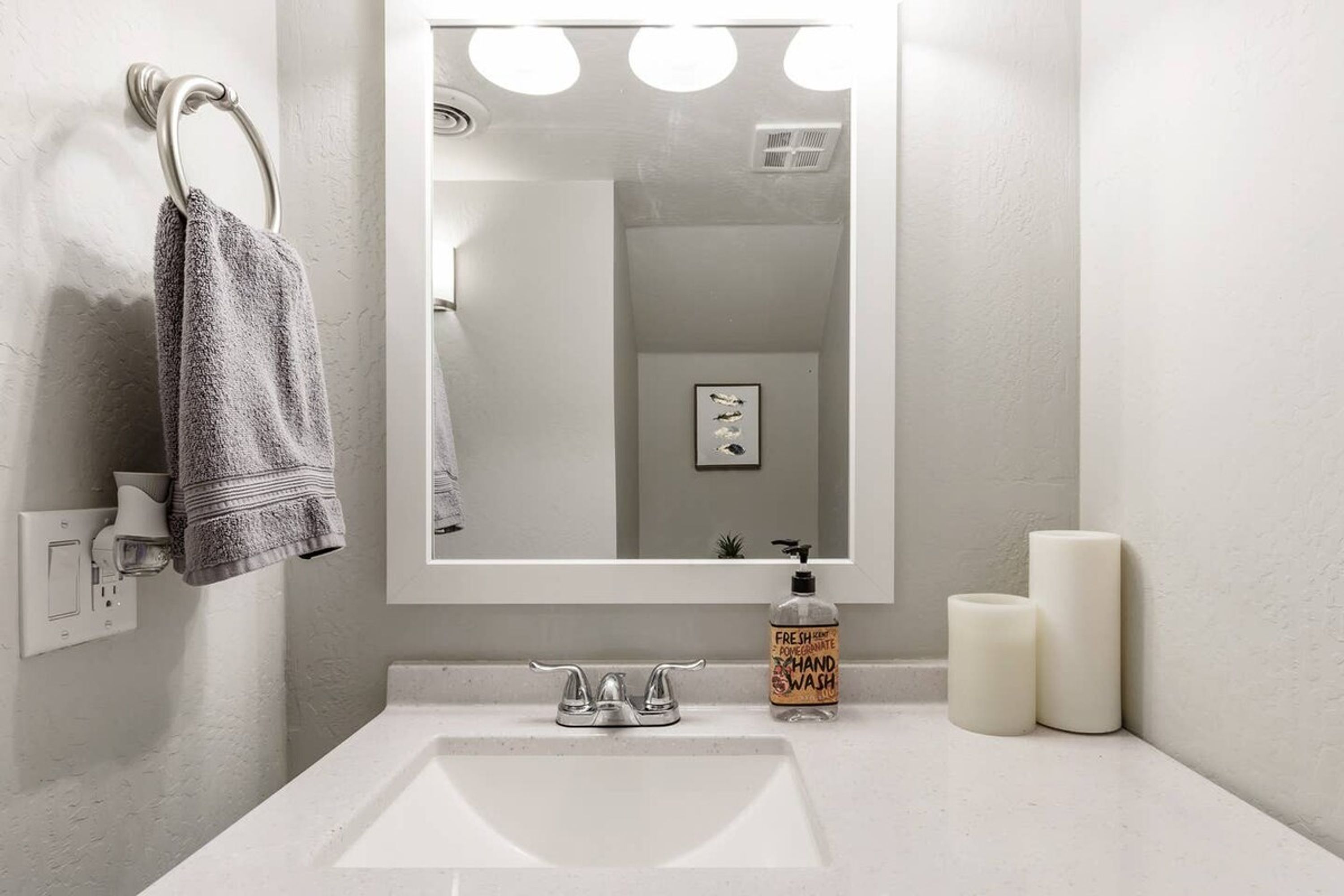 A bathroom with a white sink, a towel ring with a towel, a mirror with lights, and two candles.