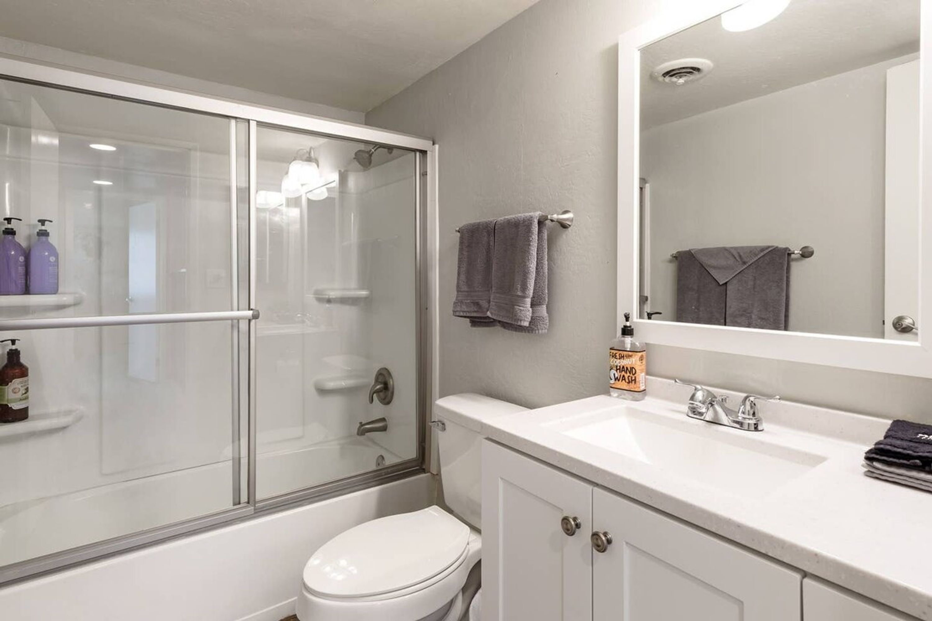 Een badkamer met een douche met glazen wand, een wit toilet, een wastafel met spiegel en toiletartikelen op het aanrecht.