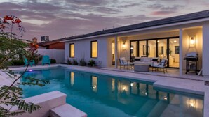 A modern house with a swimming pool, outdoor seating, and a well-lit interior. - The Kingsley Custom Heated Pool Chef Kitchen Chess (Scottsdale)
