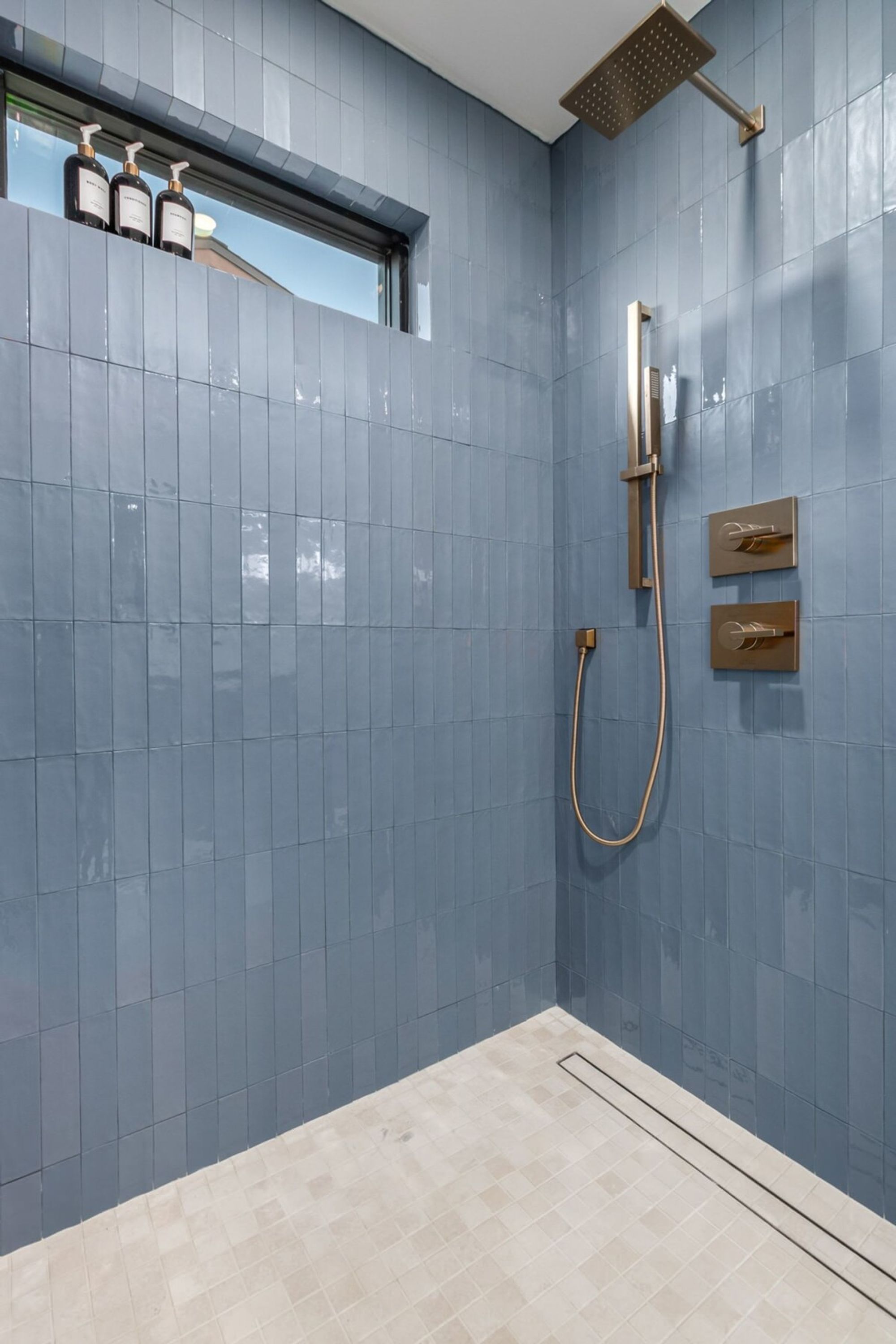 Ein modernes Badezimmer mit blauen Fliesen, einer Duschbrause und einem Fenster.