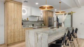 A modern kitchen with wooden cabinets, a marble island, and pendant lighting. - The Kingsley Custom Heated Pool Chef Kitchen Chess (Scottsdale)
