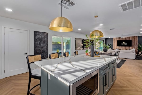 A modern kitchen with a marble island, pendant lighting, and a dining area with chairs and a table.