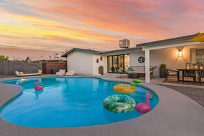 A modern house with a swimming pool, outdoor seating, and a sunset view.