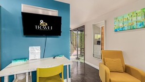 A reception area with a blue wall, a mounted TV displaying a logo, a white desk with a yellow chair, and a yellow armchair. - Coronado Casita - Mins to DT Airport Hospitals (Phoenix)