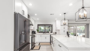 Une cuisine moderne avec des meubles blancs, un grand îlot central et des luminaires suspendus.