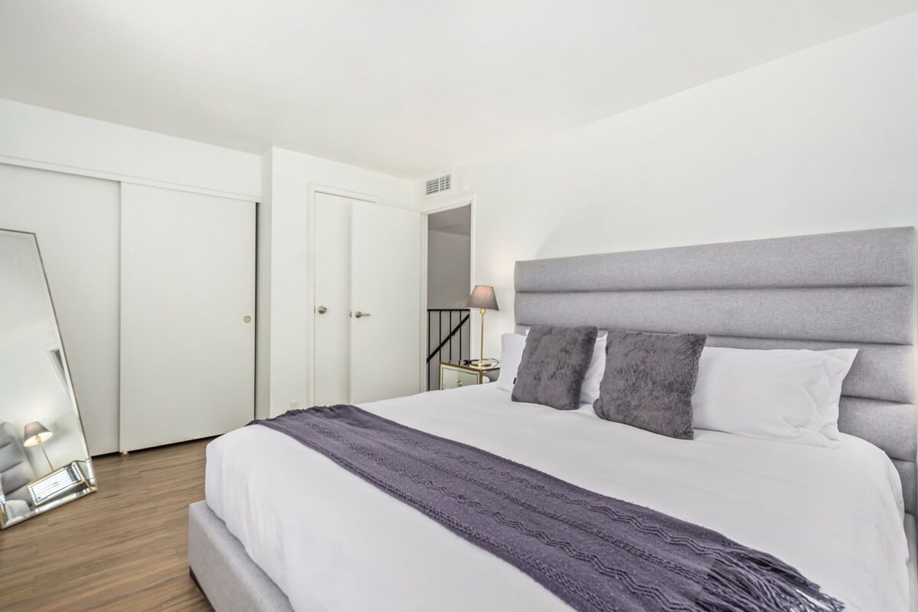 A modern bedroom with a large bed, a mirror, and a wardrobe.