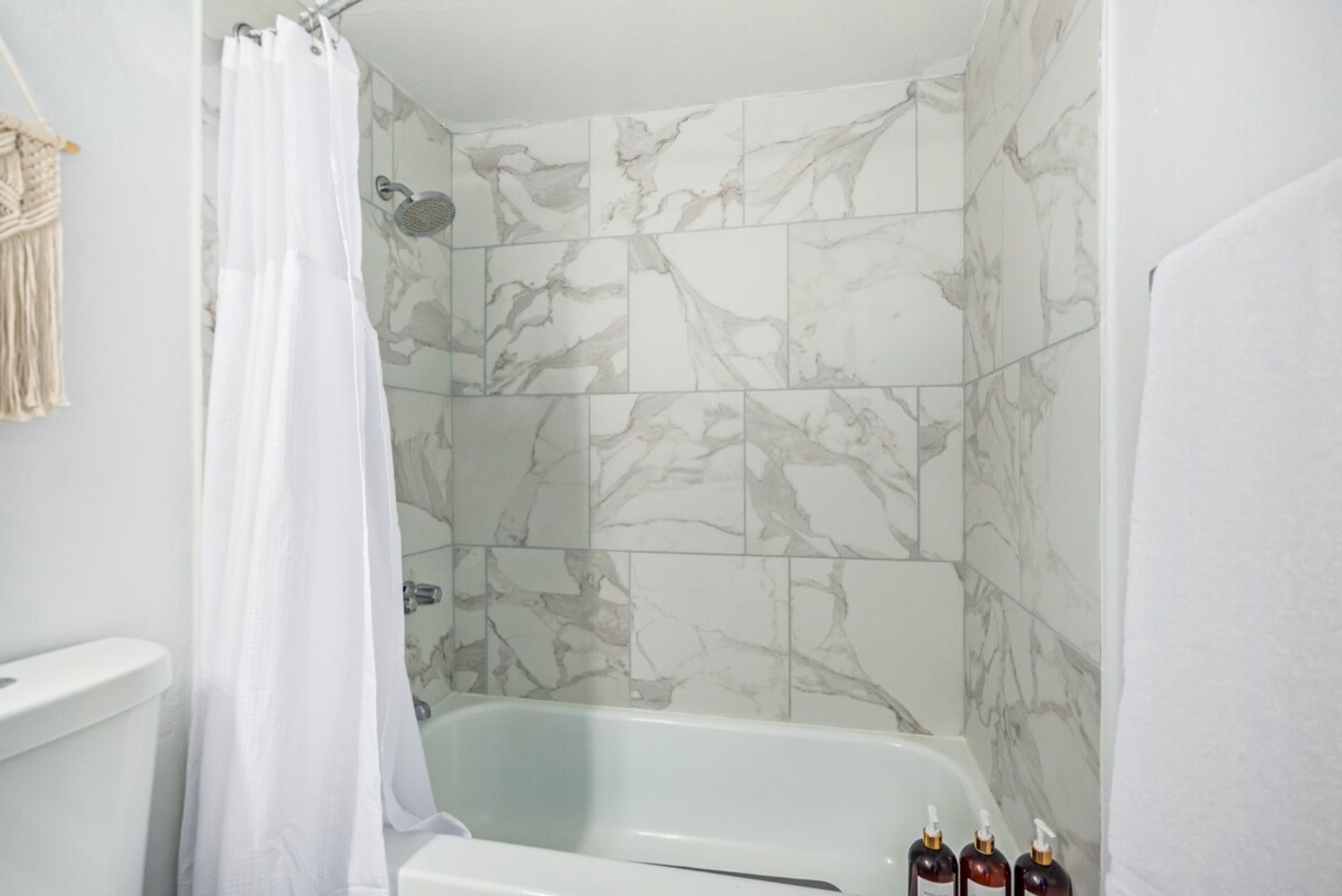 A bathroom with a white bathtub, marble tiles, and a shower curtain.