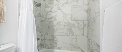 A bathroom with a white bathtub, marble tiles, and a shower curtain.