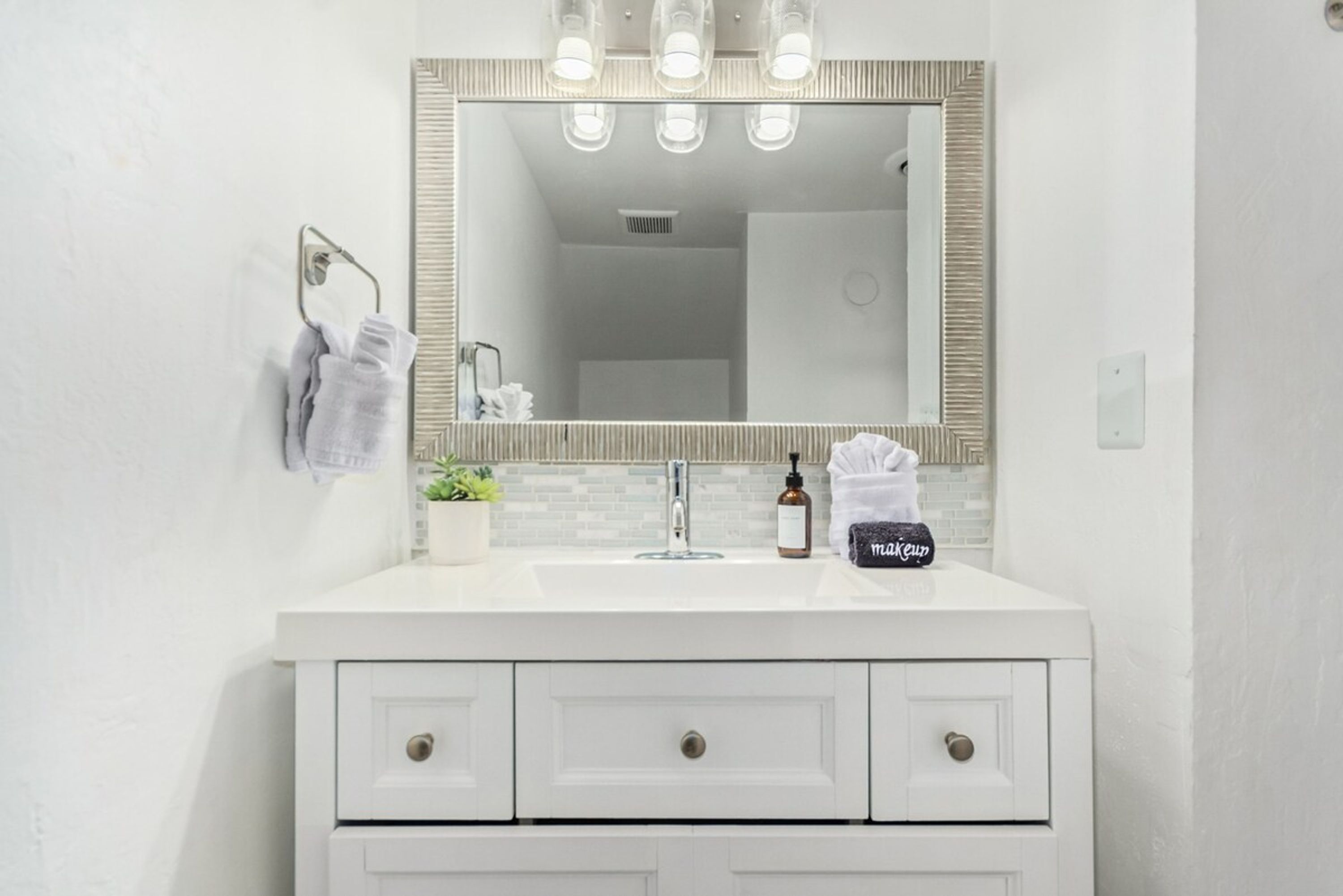 A white bathroom vanity with a large mirror, three lights above it, and a towel rack with two towels.