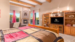 A bedroom with a large bed, wooden beams, a fireplace, a television, and a view of the outdoors. - Desert Foothils Rustic Resort Oasis w Pool Spa (Scottsdale)