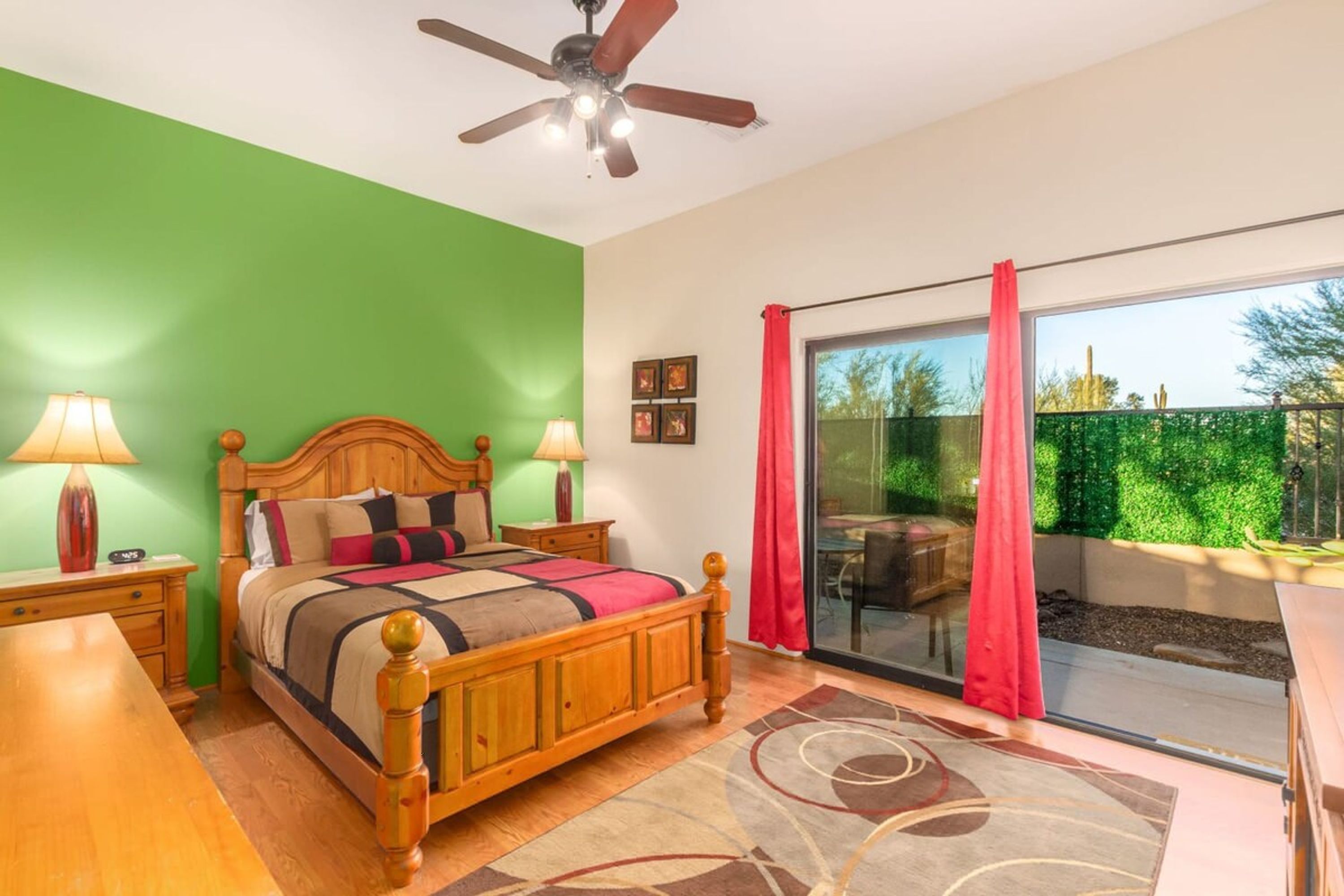 A bedroom with a wooden bed, green walls, a ceiling fan, and a view of a garden through a sliding glass door.