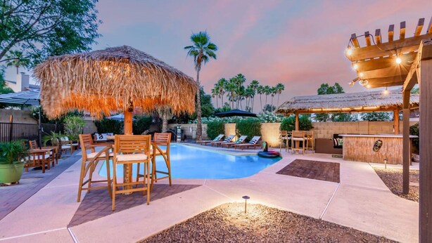 Un patio trasero con piscina, mobiliario exterior y zona de bar.