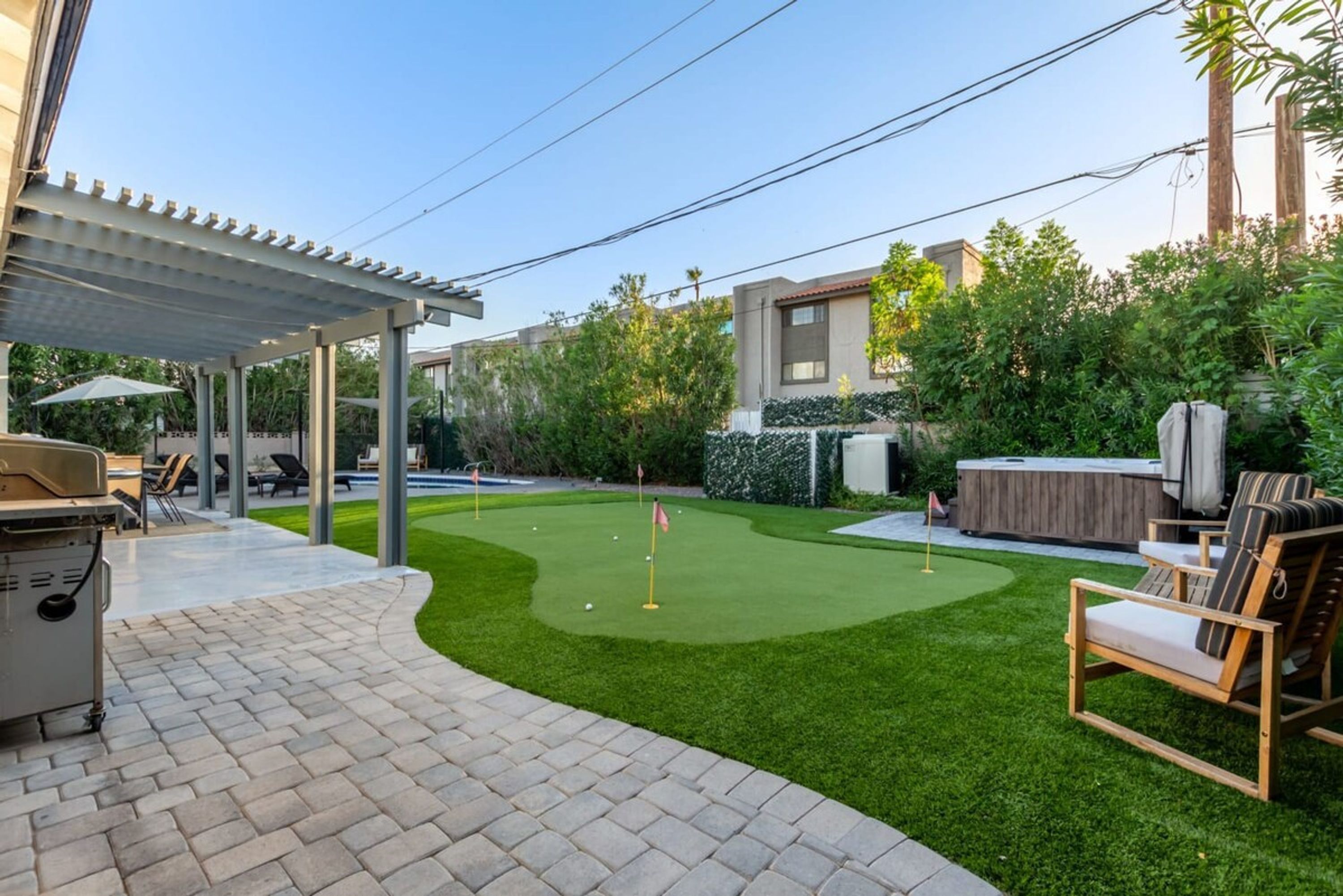 Ein Garten mit Putting Green, Gartenmöbeln und Grillplatz.