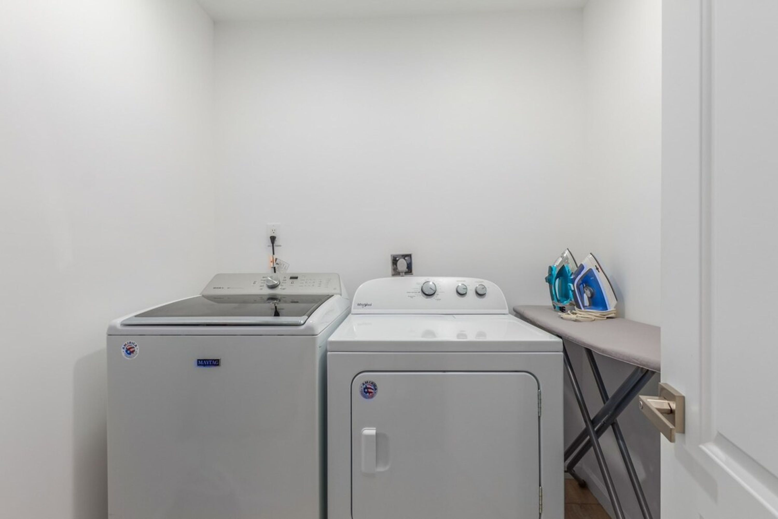 A compact laundry area with a Maytag washer and dryer, a small ironing board, and a sink.