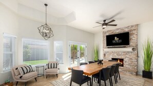 Un salon spacieux avec une table à manger en bois, des chaises noires, un canapé beige et un téléviseur fixé à un mur en pierre.