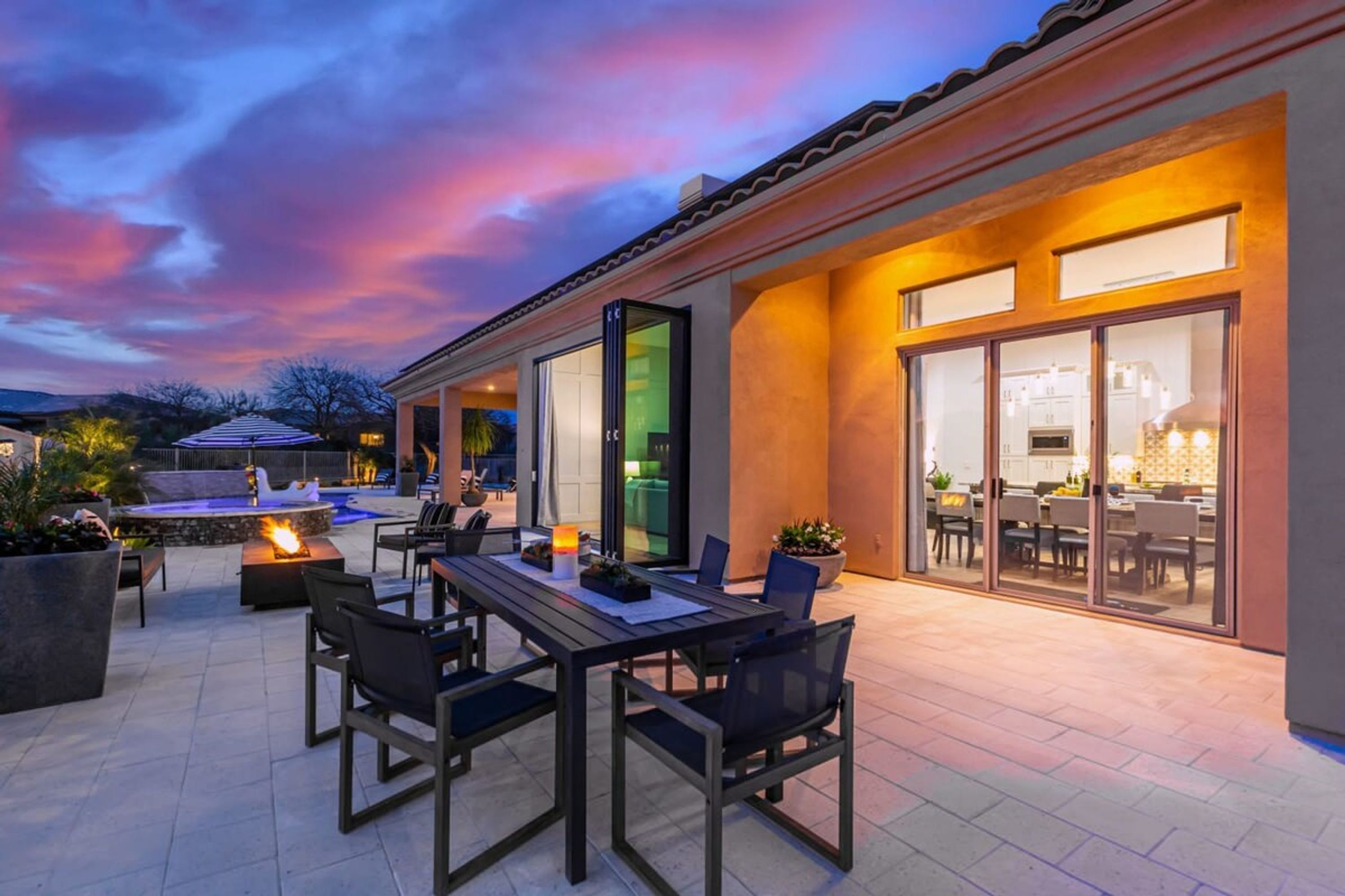 A patio with a dining table and chairs, a fire feature, and a view into the house.