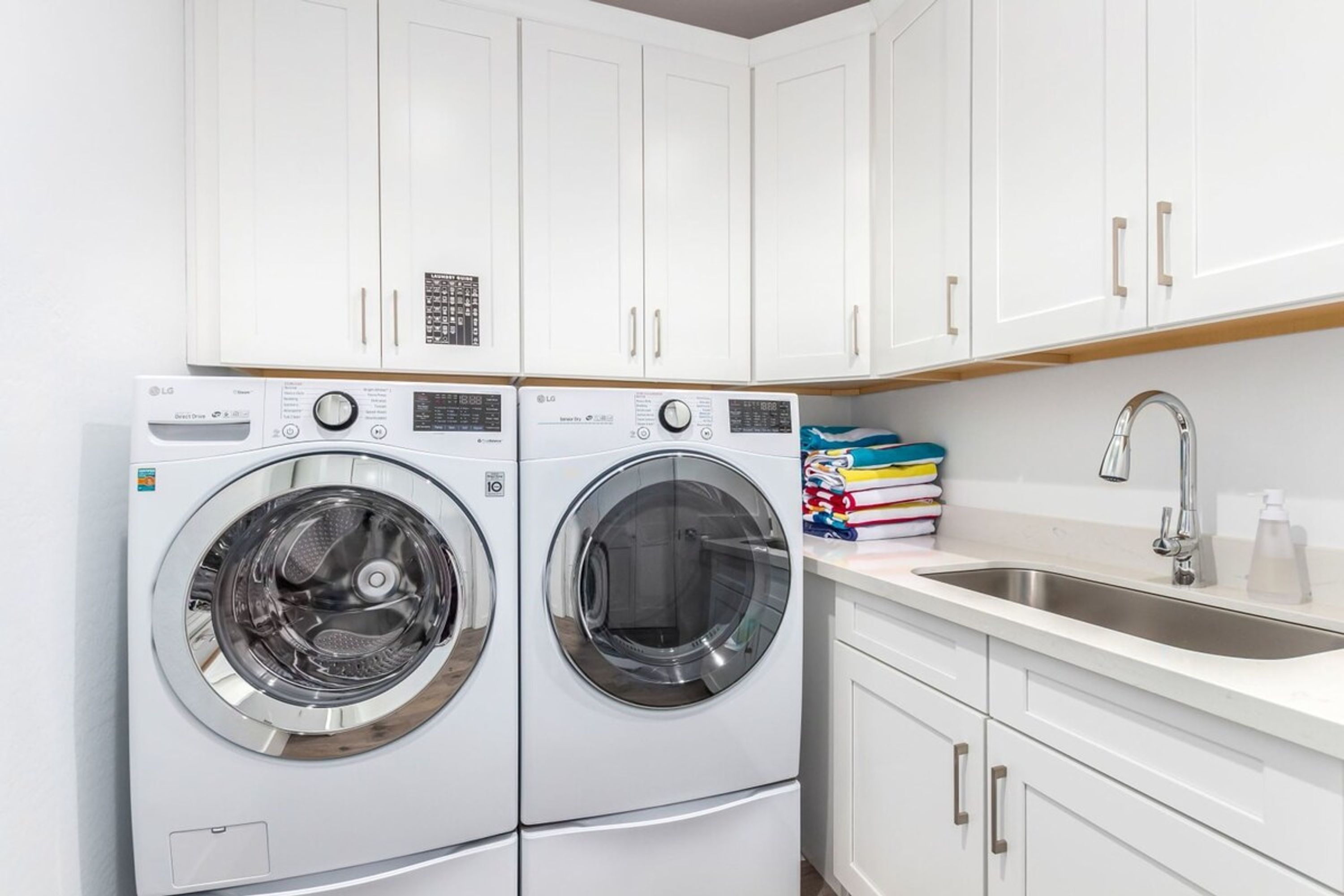 A laundry area with two white washing machines, a sink, and a stack of colorful laundry detergent boxes.