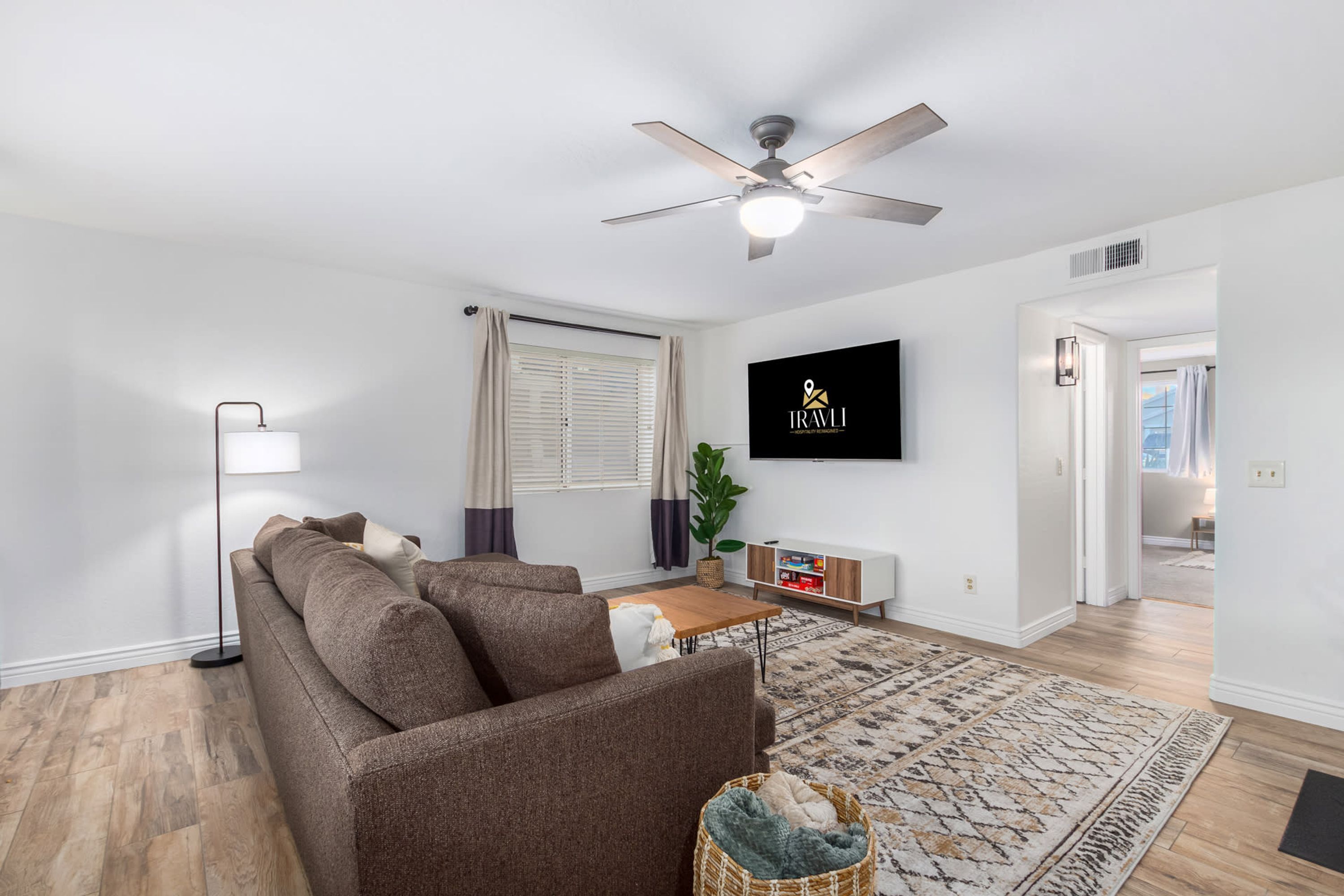 A modern living room with a brown sofa, a floor lamp, a TV mounted on the wall, and a ceiling fan.