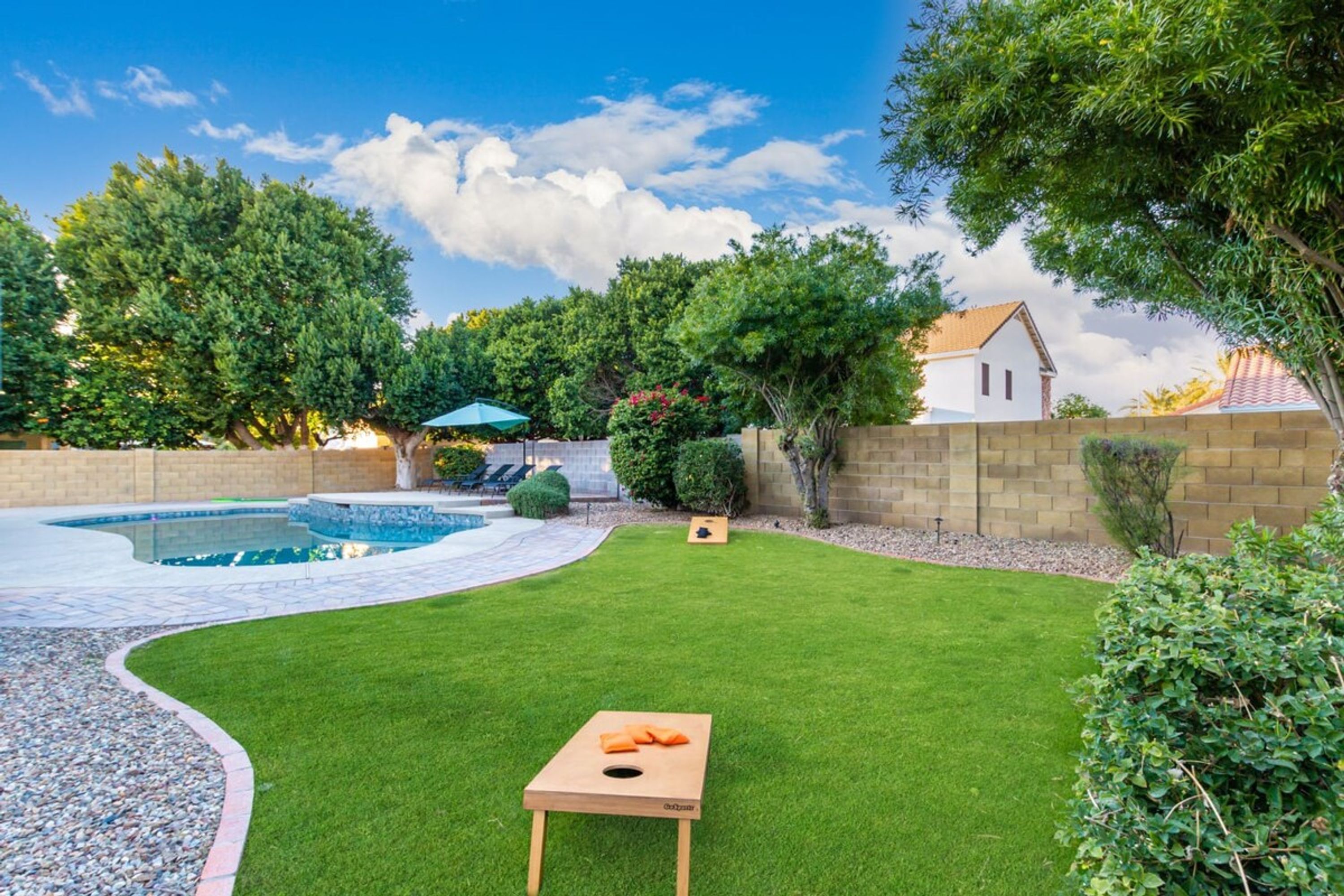 A backyard with a swimming pool, a wooden table, and a lawn.