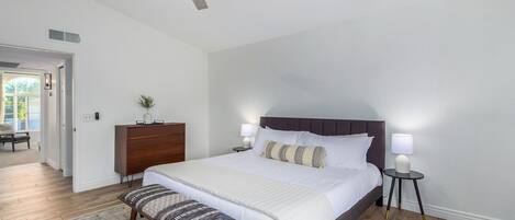 A bedroom with a large bed, a ceiling fan, a nightstand, a dresser, and a bench.