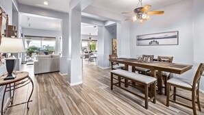 A spacious dining area with a wooden table and chairs, a ceiling fan, and a view of the kitchen in the background. - Sunset View Retreat Pool Spa Amazing Views (Scottsdale)