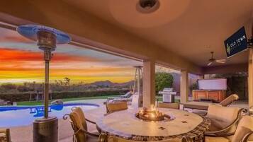 Um pátio com uma mesa redonda, cadeiras, lareira e vista para uma piscina e montanhas.