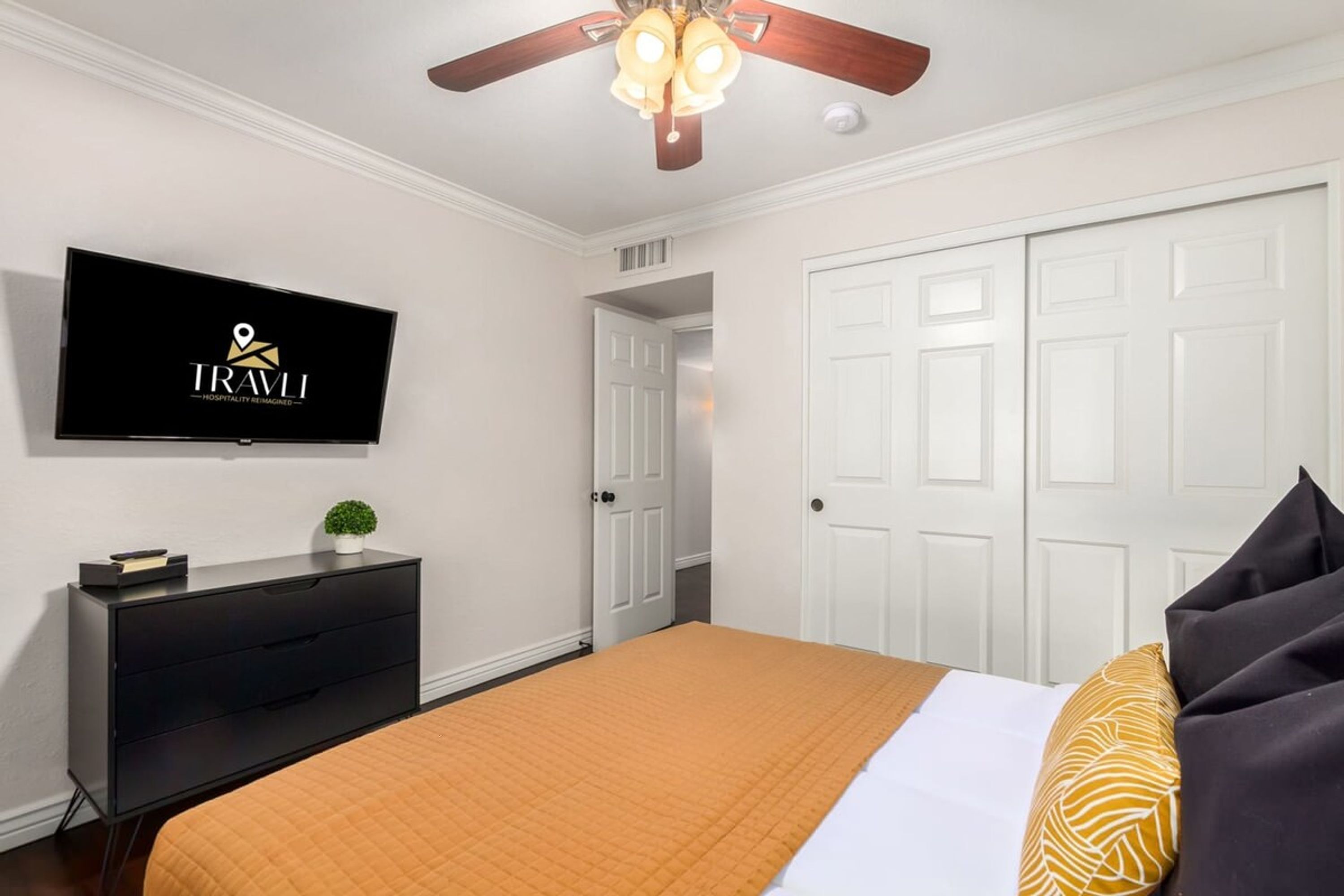 Une chambre d’hôtel avec un lit, un téléviseur fixé au mur, un ventilateur de plafond et une porte.