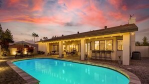 Une piscine à bord incurvé, entourée d’un patio aménagé avec des espaces de détente en plein air et une partie couverte.