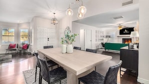 Un salon spacieux avec une grande table à manger en bois, des chaises noires en osier et une cheminée. On y trouve plusieurs portes et un mur d’accent de couleur verte.