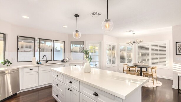 Une cuisine moderne avec des meubles blancs, un îlot central et des luminaires suspendus.