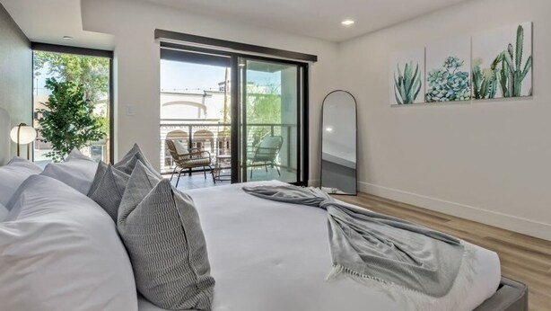A modern bedroom with a large bed, a sliding glass door to a balcony, and a cactus wall art piece. - LUX City View Studio Old Town Gym Balcony (Scottsdale)