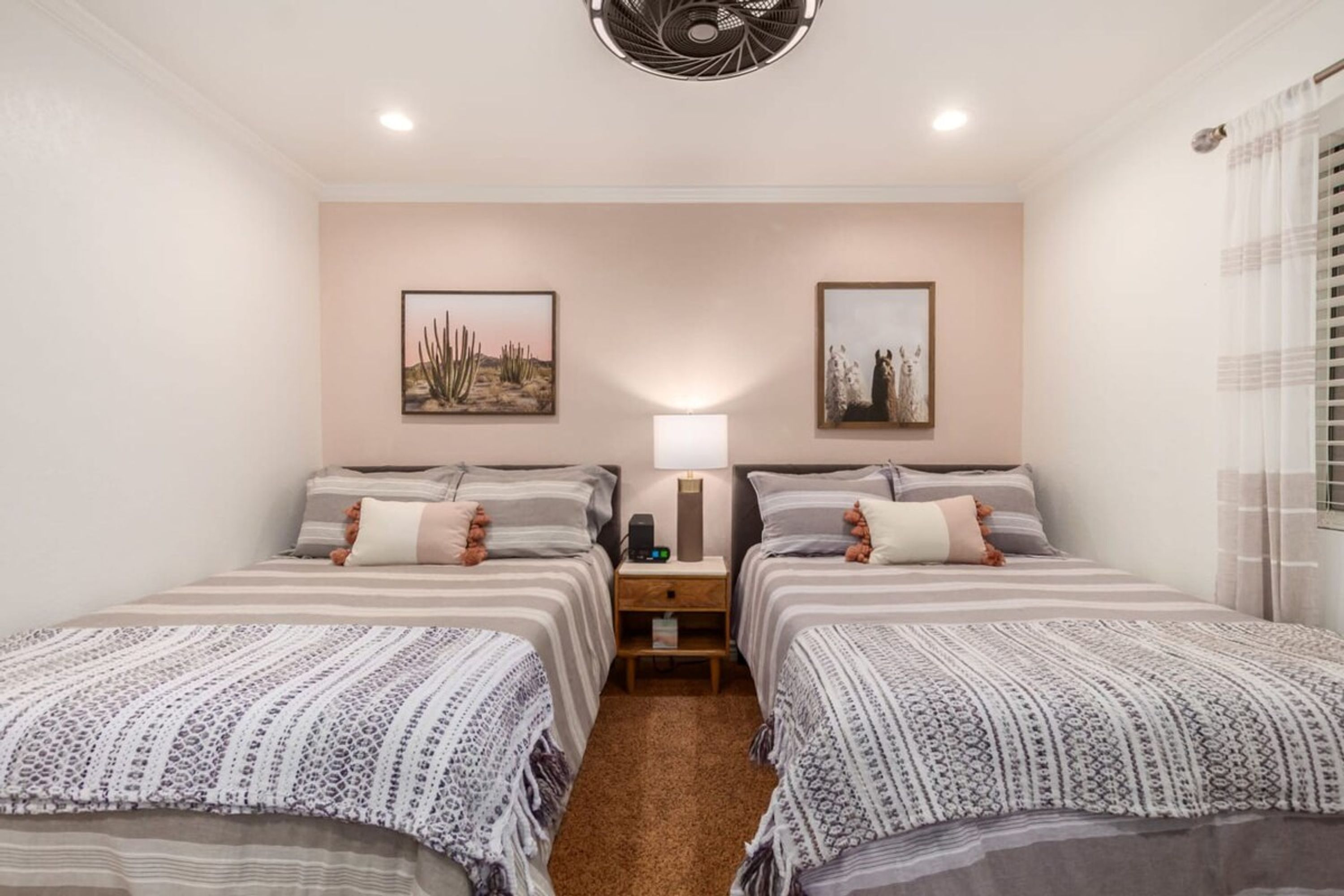 Une chambre d’hôtel avec deux lits, une table de chevet, une lampe et deux tableaux encadrés au mur.
