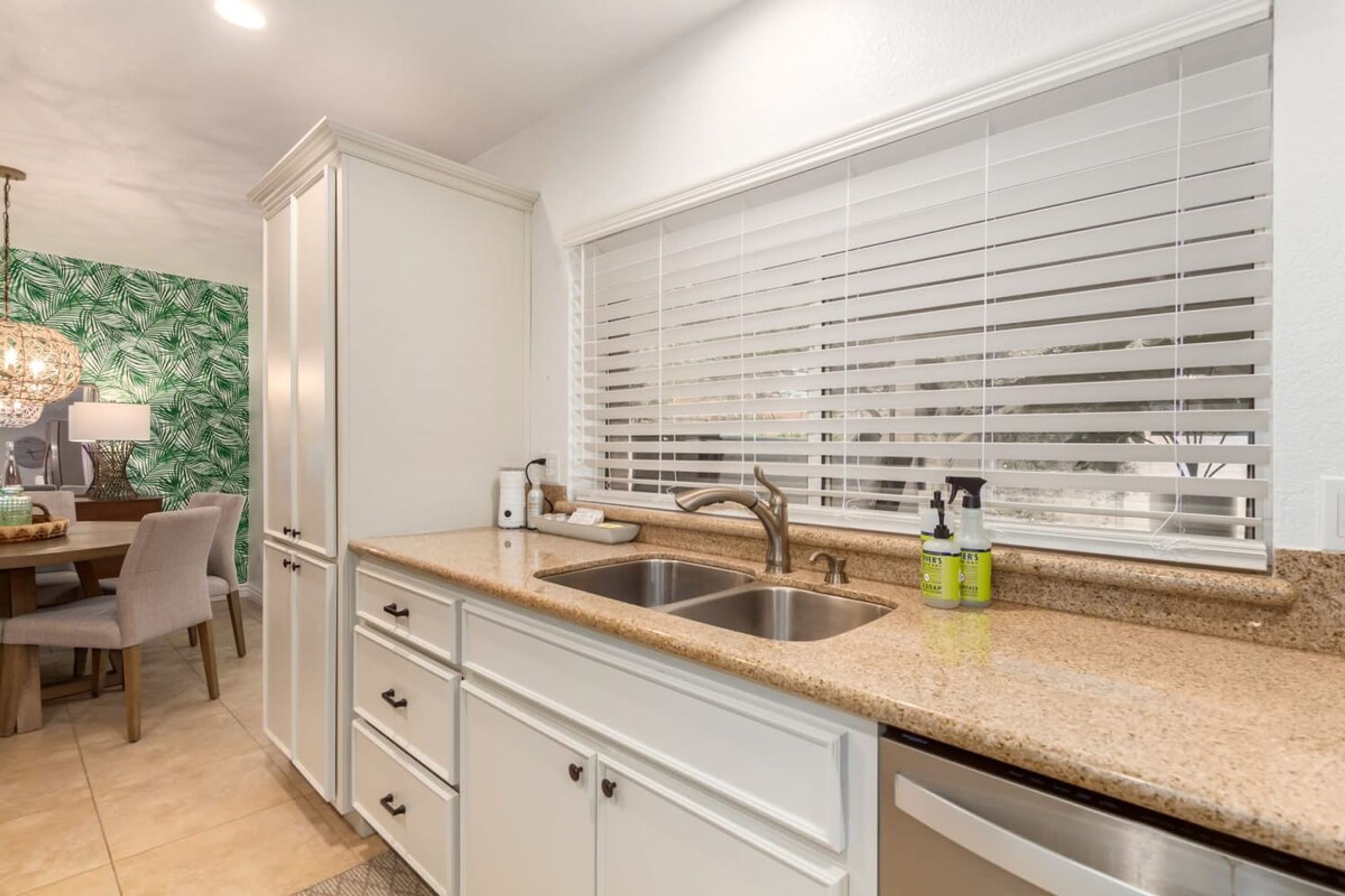 A kitchen with white cabinets, a granite countertop, a double sink, and a window with blinds.