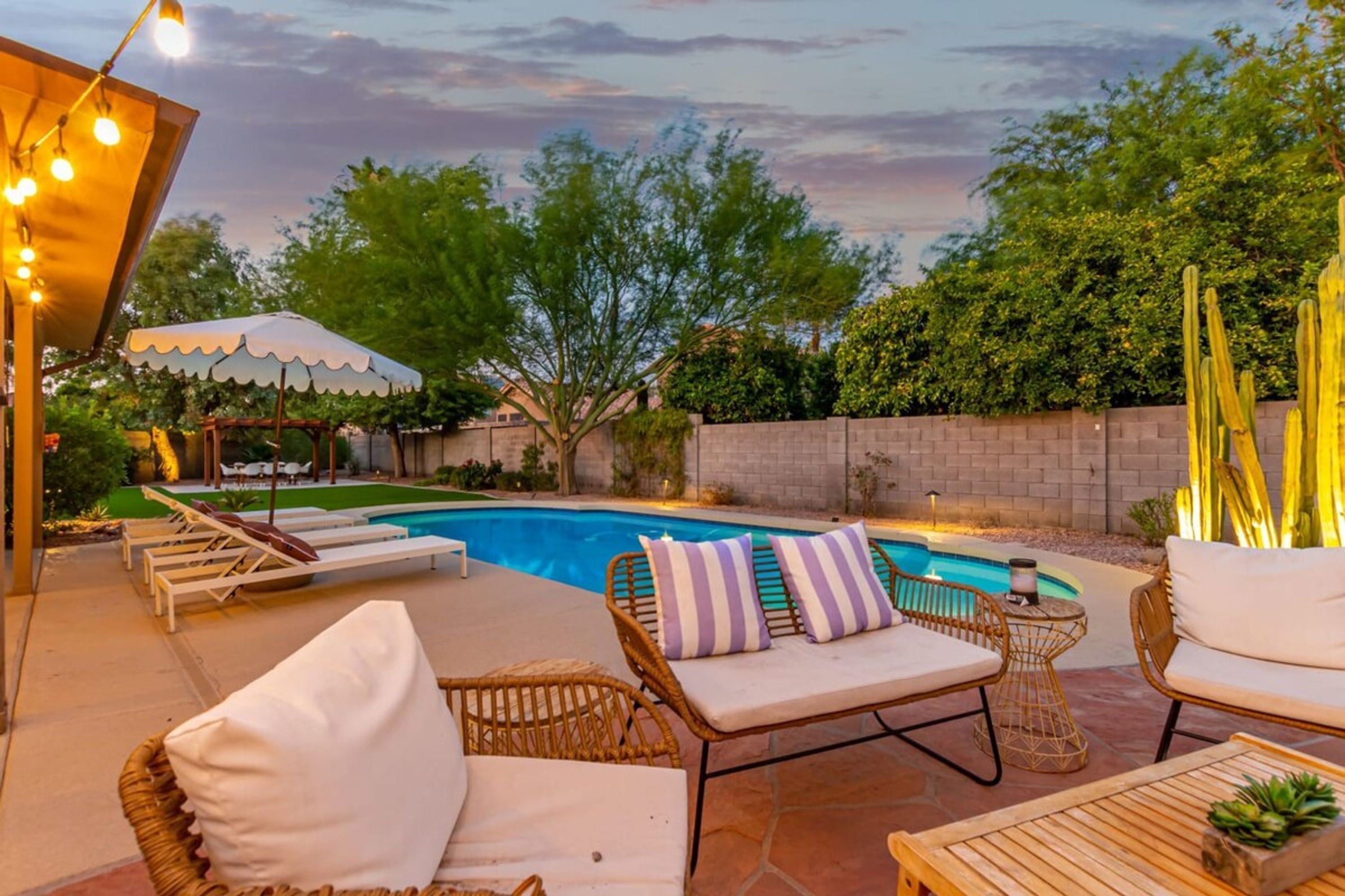 A poolside area with lounge chairs, a table, and a pergola with string lights.