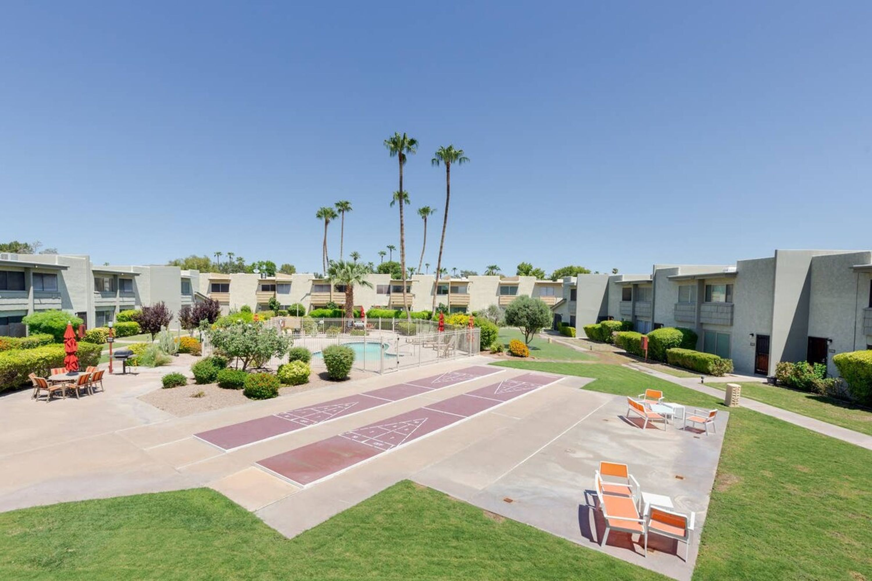 A courtyard with a shuffleboard court, outdoor seating, and a pool.