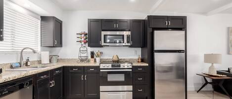 A modern kitchen with black cabinets, stainless steel appliances, and a granite countertop.