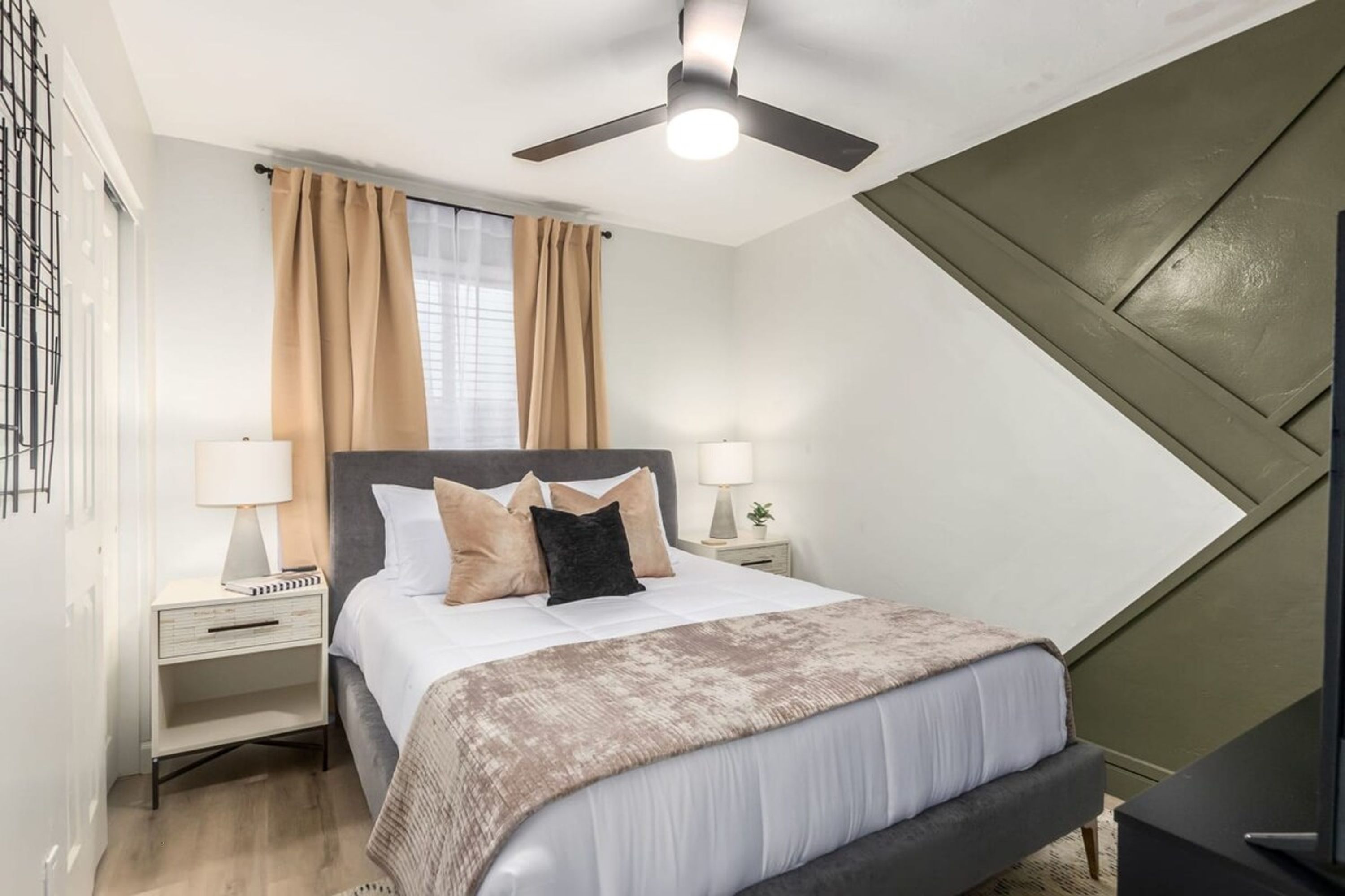 A modern bedroom with a bed, nightstands, a ceiling fan, and a window with curtains.