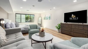 Uma sala de estar moderna com um sofá cinzento, uma mesa de centro redonda, uma poltrona cinza e uma televisão em um aparador de madeira.