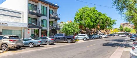 A street view with parked cars, a building with balconies, and trees.