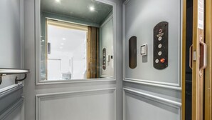 Um elevador moderno com painel de controle, porta de vidro e vista para o corredor.