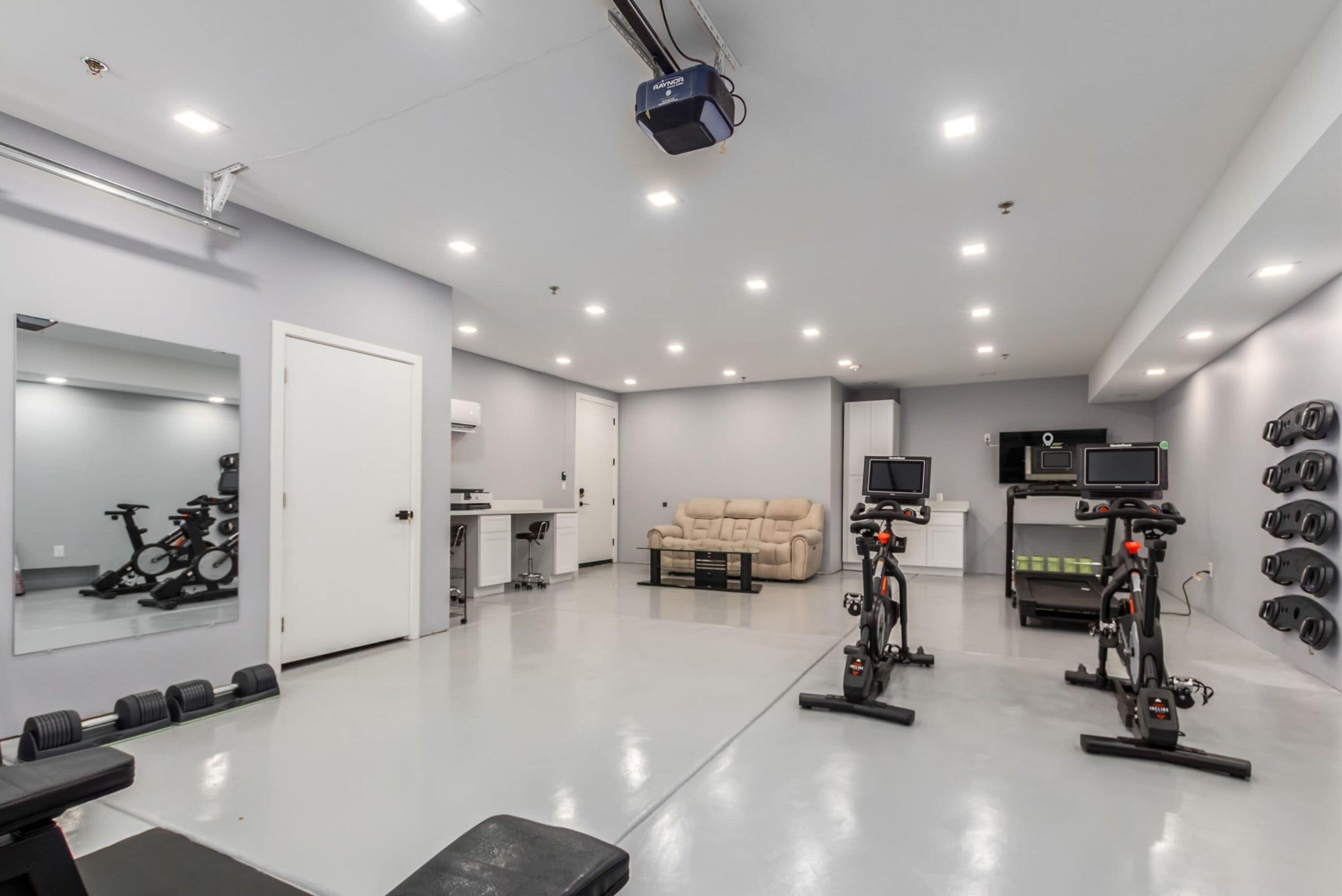 A modern gym with exercise equipment, a mirror, and a sofa.