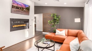 A modern living room with a fireplace, orange sofa, and a large plant. - Broadway Palms Private Pool Chef Kitchen Office (Tempe)