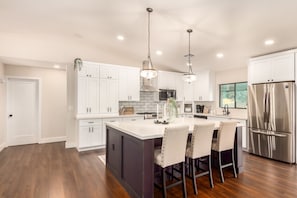 A modern kitchen with white cabinets, stainless steel appliances, and a central island with bar stools. - Broadway Palms Private Pool Chef Kitchen Office (Tempe)