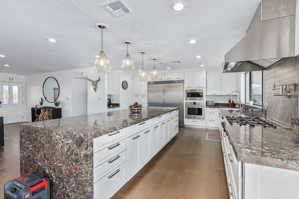 A modern kitchen with white cabinetry, granite countertops, stainless steel appliances, and pendant lighting.