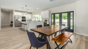 A modern kitchen with white cabinets, a central island, and a dining area with a wooden table and chairs. - Modern Arcadia Estate Htd Pool Bikes Chef Kitchen (Phoenix)