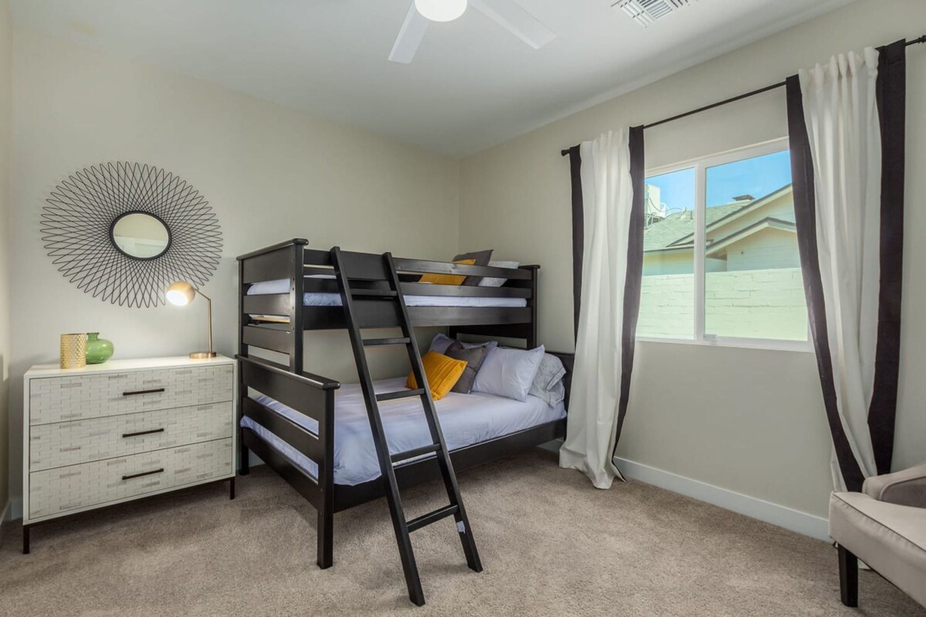 A bedroom with a bunk bed, a dresser, a mirror, and a window with curtains.
