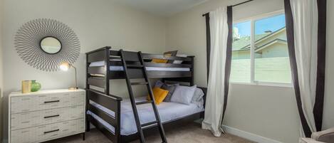 A bedroom with a bunk bed, a dresser, a mirror, and a window with curtains.