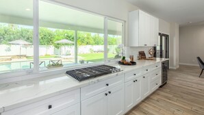 A modern kitchen with white cabinetry, a large window overlooking a backyard, and a built-in stove. - Modern Arcadia Estate Htd Pool Bikes Chef Kitchen (Phoenix)