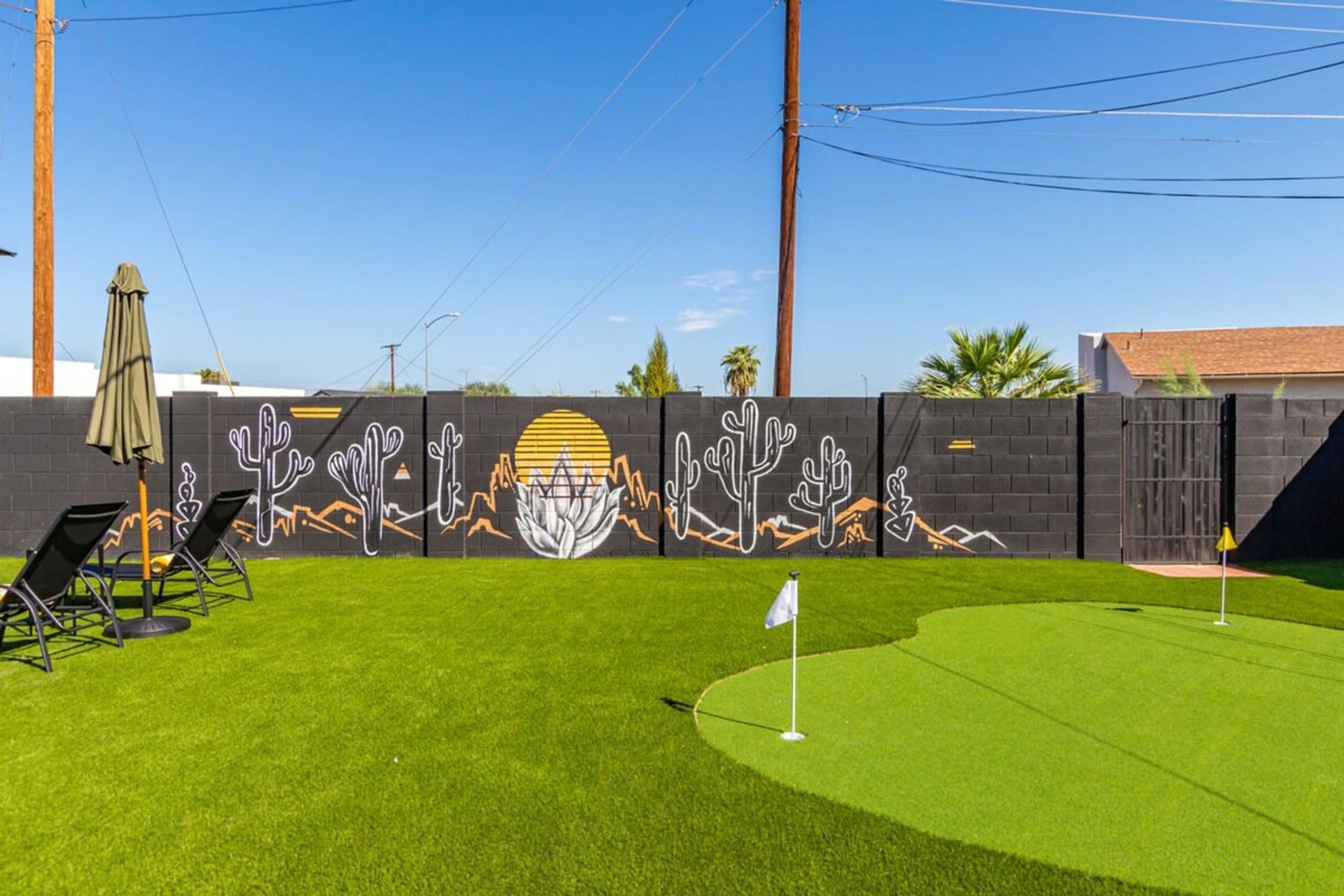 Un césped bien cuidado con un hoyo de golf, un mural de cactus y una valla.
