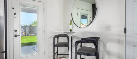 A modern kitchen with a refrigerator, a dining table with two chairs, and a large mirror on the wall.